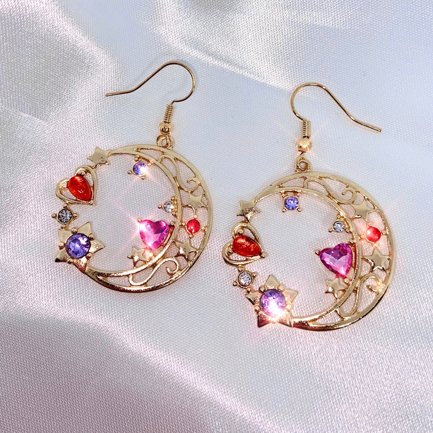 white backdrop with gold crescent moon earrings in drop style and multicoloured heart accents