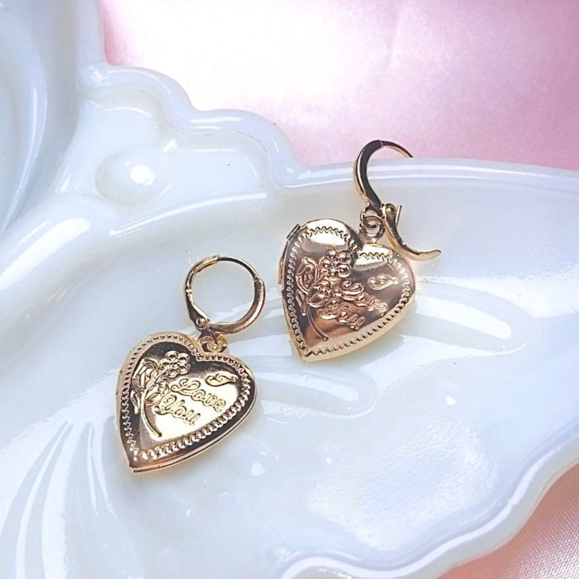 two drop locket earrings shaped in a heart with gold hardware on a butterfly tray