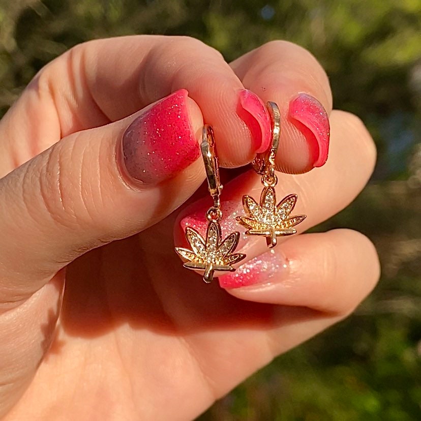 two gold marijuana drop earrings held in hand