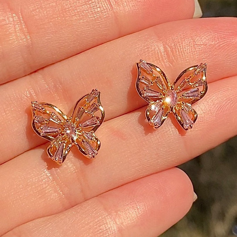two butterfly stud earrings with cubic zirconia laying flat on hand
