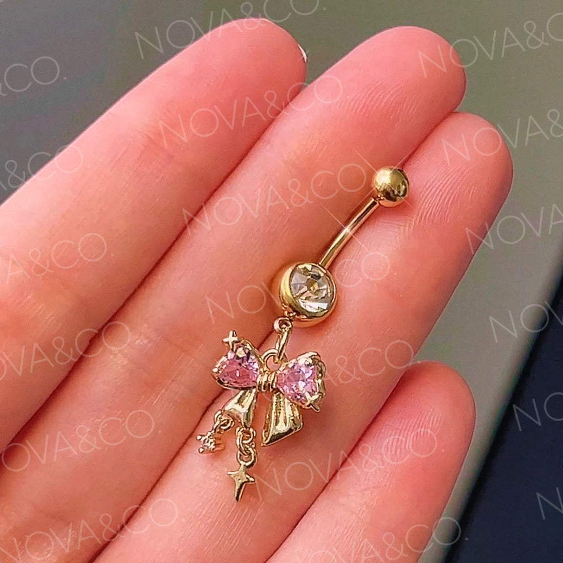 Gold bow belly button ring with pink and clear cubic zirconia, featuring dangle sparkle charms. Coquette style.