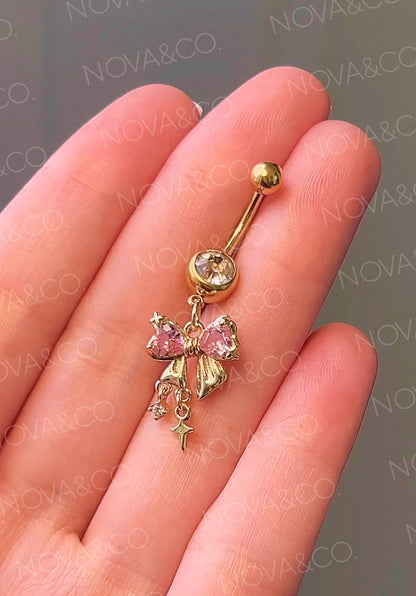 Gold bow belly button ring with pink and clear cubic zirconia, featuring dangle sparkle charms. Coquette style.