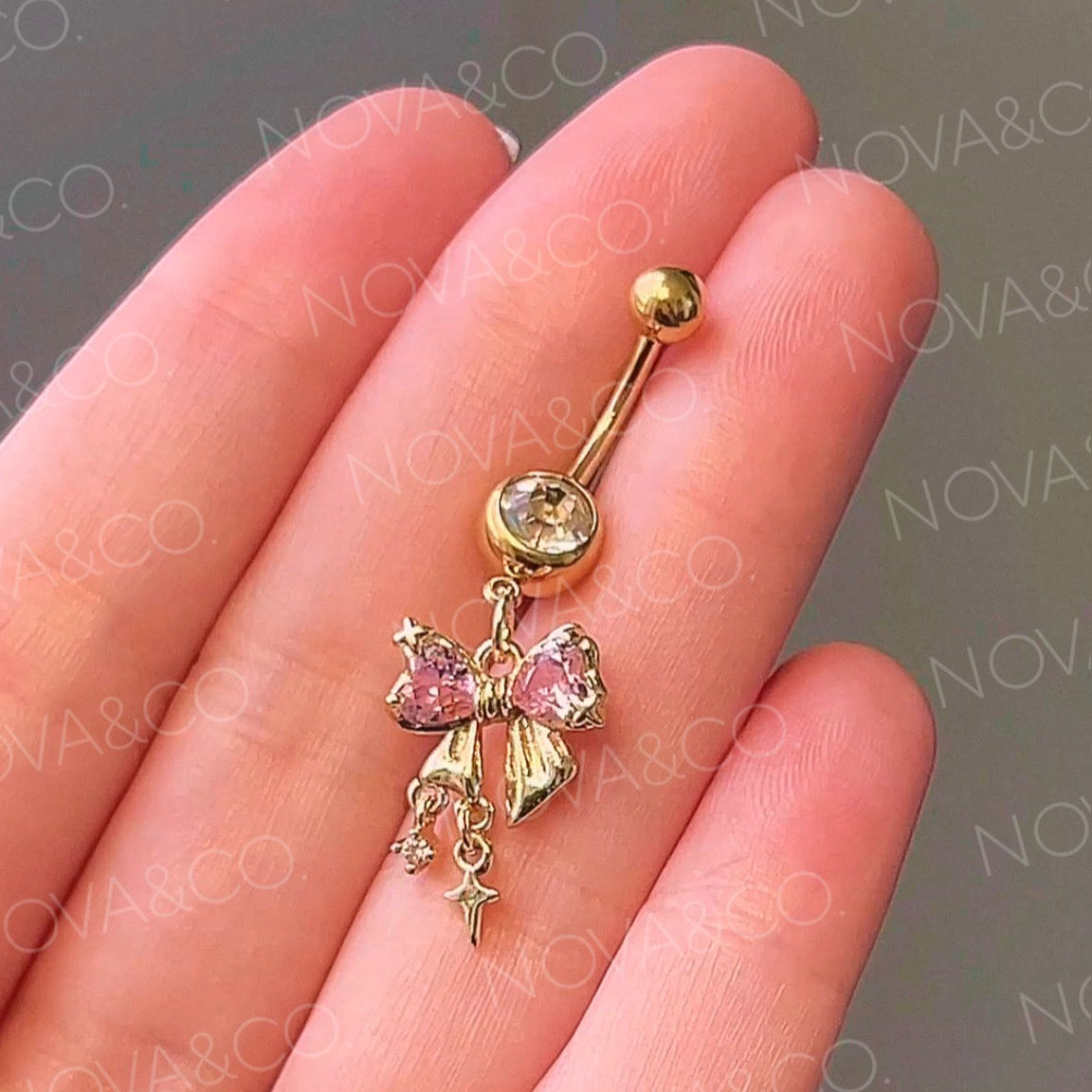 Gold bow belly button ring with pink and clear cubic zirconia, featuring dangle sparkle charms. Coquette style.