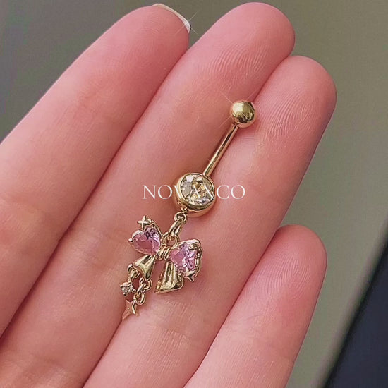 Gold bow belly button ring with pink and clear cubic zirconia, featuring dangle sparkle charms. Coquette style.