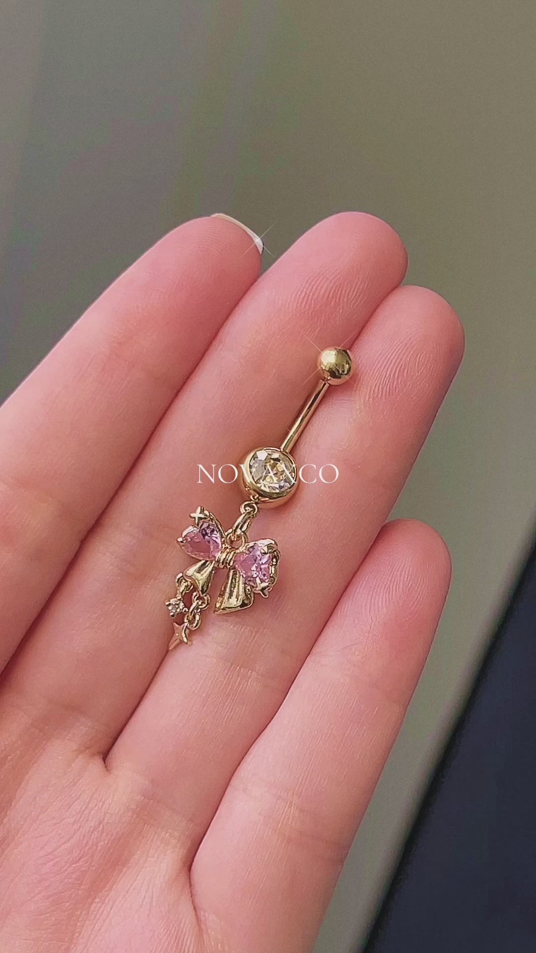 Gold bow belly button ring with pink and clear cubic zirconia, featuring dangle sparkle charms. Coquette style.