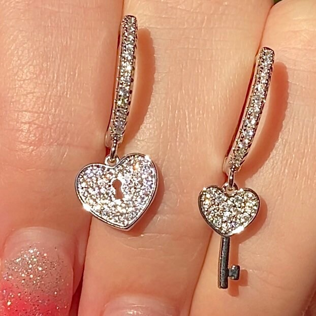 assymetrical heart and lock hoop huggie earrings with cubic zirconia encrusted sitting in fingers