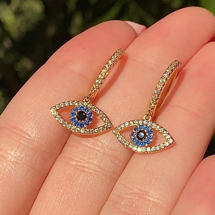 gold evil eye earrings covered in cubic zirconia gemstones held in fingers 